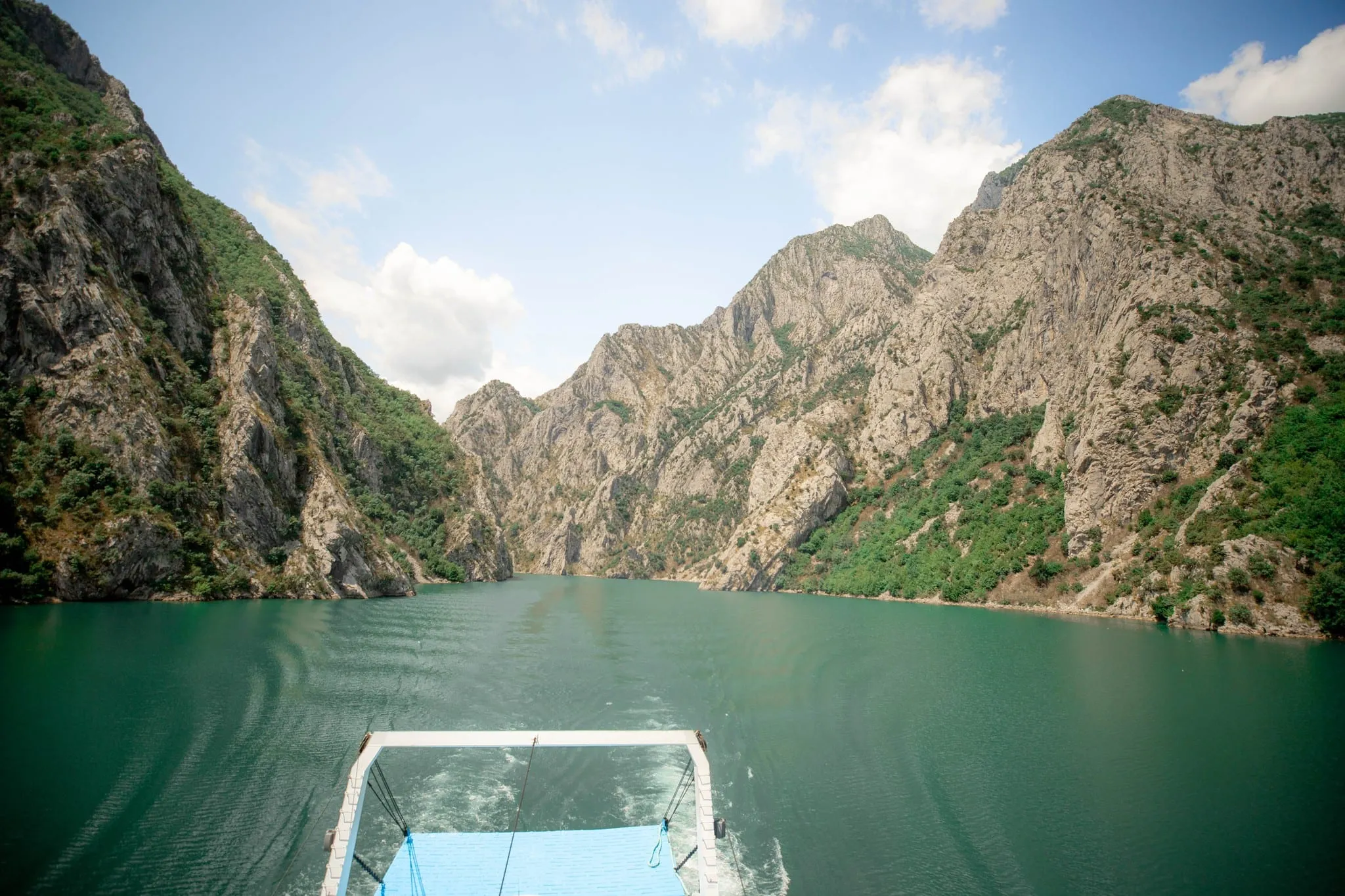 View from the bow of a ferry gliding over turquoise water through the steep, rocky canyon of Komani Lake in northern Albania