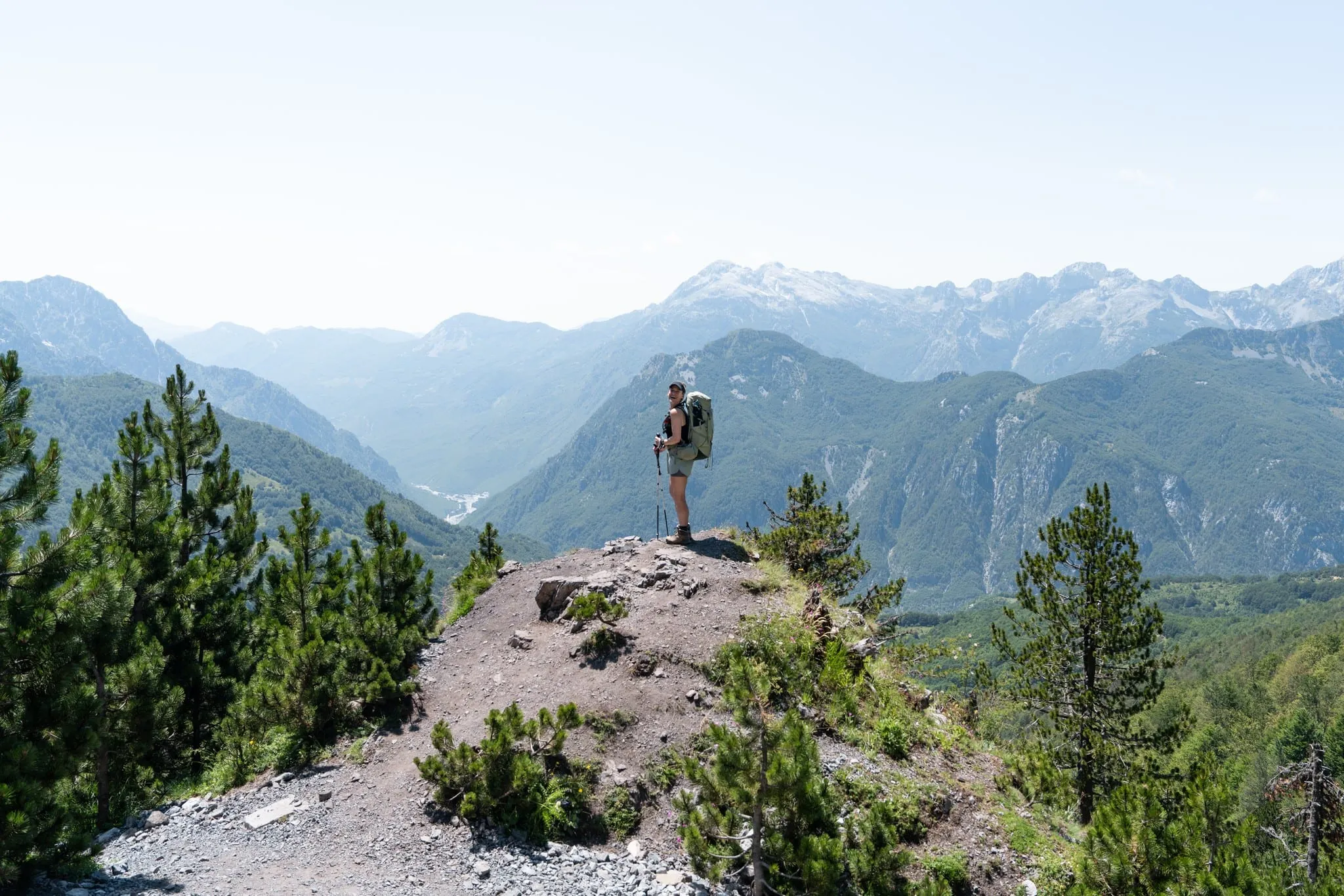 Een wandelaar op een rotsige bergkam kijkt uit over rijen groene bergen op de grens tussen Albanië en Montenegro