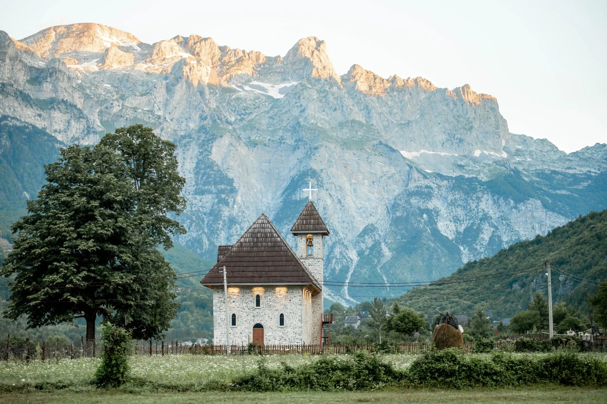 De stenen kerk van Theth met haar klokkentoren voor de kalksteenbergen bij zonsondergang