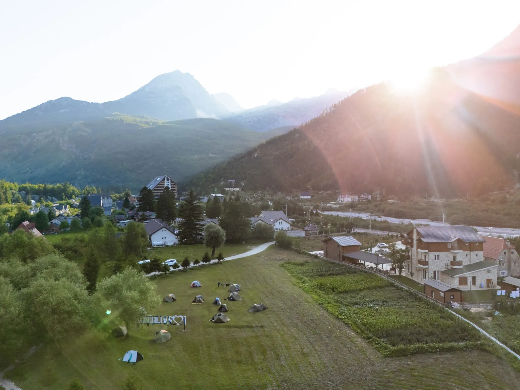 Dronebeeld van tenten op een groen veld naast guesthouses in het dal van Valbonë bij zonsondergang